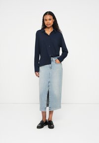 Camisa azul-marinho de manga comprida com botões, saia maxi de denim clara com fenda frontal, sapatos mocassins pretos. Tecido suave e design de corte reto.