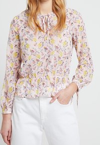 Blusa rosa con motivo floreale, con vita arricciata e maniche lunghe. Il materiale sembra leggero e texturizzato.