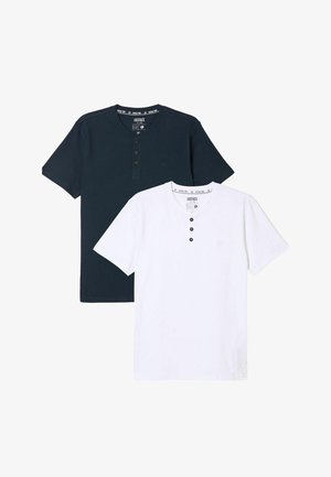 Marineblaue Henley-T-Shirt mit kurzen Ärmeln und drei Knöpfen, kombiniert mit dunkelblauen Denim-Jeans und olivgrünen Sneakers. Einfarbiger Hintergrund.