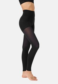 Schwarze hochtaillierte Leggings mit einem transparenten Einsatz am Unterschenkel. Glatte Textur, körpernahe Passform und minimales Branding am Bund.