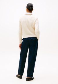 Crème gebreide trui met een gestructureerd patroon; marineblauwe broek met een rechte snit en omgeslagen mouwen; zwarte instappers.
