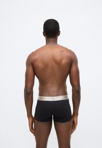 Fekete szövet boxerek bézs derékrésszel, szoros illeszkedéssel és sima textúrával. A modell hátulról látható.