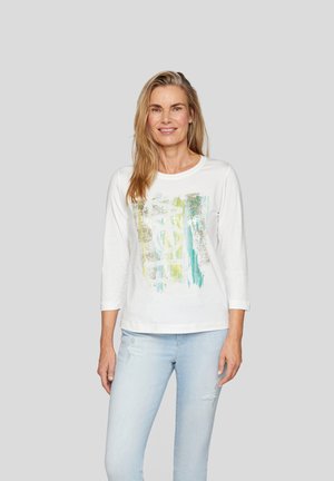 White cotton shirt with three-quarter sleeves, featuring a colorful abstract print in green and blue. Worn with light blue distressed jeans.