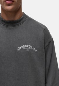 Grijze sweatshirt met een hoge hals. Heeft een wit tekstlogo "GOOD FOR NOTHING" en "2011" in een gebogen ontwerp. Zachte textuur.
