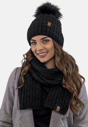 Berretto lavorato a maglia nero con pom-pom e sciarpa nera coordinata. Entrambi presentano un motivo testurizzato e un piccolo etichetta con logo marrone.
