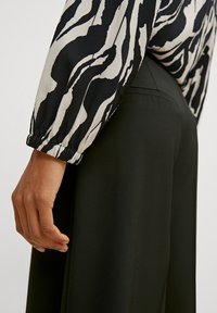 Haut à manches longues noir et blanc avec un motif ondulé, assorti à un pantalon noir taille haute. Les manches disposent de poignets élastiques.