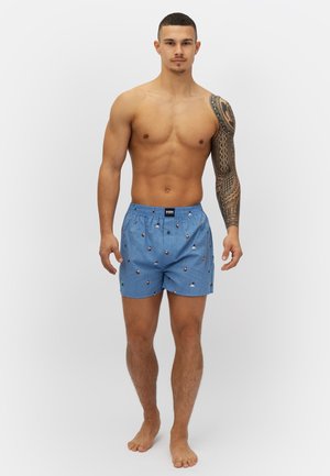 Boxers bleus à motifs avec un tissu léger ; présente de petits motifs colorés d'arbres et de personnes ; taille élastique, coupe décontractée.