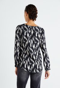 Zwart-wit geblokte blouse met lange, opgeblazen mouwen en een ronde halslijn, voorzien van een ritssluiting aan de achterkant en een losse pasvorm.