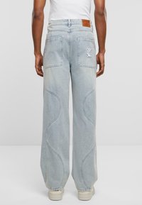 Pantalones de mezclilla de pernera ancha en azul claro con dos bolsillos traseros, costuras curvas y un parche de cuero marrón en la cintura.