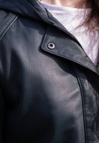 Dark blue leather jacket with a smooth texture, featuring a flap collar, button fastening, and visible stitching details.