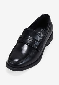 Mocasín de cuero negro con puntera redondeada, que presenta una tira y un detalle de botón en la parte superior. Superficie texturizada y tacón bajo de goma.
