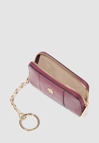 Burgundy leather wallet with a gold zipper, chain keyring, and beige interior lining. Features a smooth texture and a logo accent.