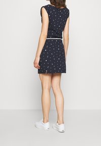 Nawojęto sukienka w granatowym kolorze z krótkimi rękawami i białymi wzorami kwiatowymi, ściągnięta w talii paskiem; zestawiona z białymi trampkami.