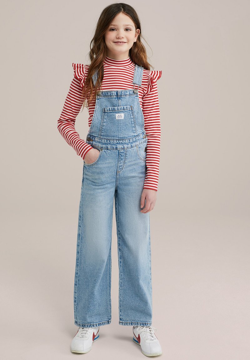 Overoles de mezclilla con corte de pierna ancha, lavado azul claro, tirantes ajustables, bolsillo frontal, combinados con una camisa de manga larga a rayas rojas y blancas.