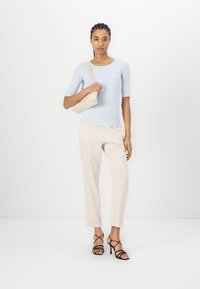 Lichtblauw fitted top, crèmekleurige tapered broek en zwarte strap heels. Het model houdt een kleine beige tas vast. Gladde texturen en een casual ontwerp.