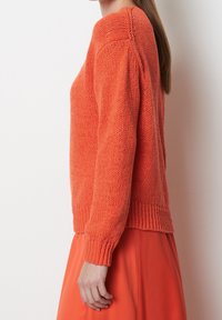 Sweter dzianinowy w jasnym pomarańczowym kolorze, o luźnym kroju, z prążkowanymi mankietami i dołem. Posiada teksturowany materiał, okrągły dekolt i długie rękawy.