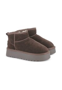 Botas de ante marrón hasta el tobillo con un forro suave, punta redondeada y suela gruesa gris. Presentan costuras mínimas y una lengüeta en la parte posterior.
