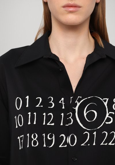 Schwarzes Hemd mit einem knopfbaren Design, das kontrastierende weiße Druckzahlen und eine umrandete '6' auf der Vorderseite aufweist. Glatte Textur, klassischer Kragen.