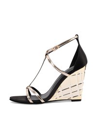 Sandalo con zeppa nera e cinturini metallici dorati, caratterizzato da un design del tacco scultoreo unico e una parte superiore in morbido materiale scamosciato.