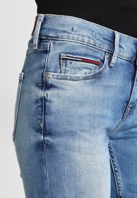 Vaqueros de mezclilla azul claro con una cintura de altura media, un ligero desvanecimiento, cuatro bolsillos y costuras rojas y azules en el bolsillo delantero.