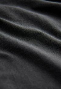 Zwarte stof met een zachte, gestructureerde oppervlakte, voorzien van zachte golven en variaties in licht, die duiden op een lichtgewicht en flexibel materiaal.