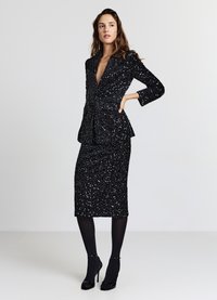 Blazer nero con paillettes e scollo a V profondo, abbinato a una gonna aderente nera con paillettes. Texture liscia, design strutturato, maniche lunghe.