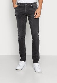 Svarta denimjeans med slim fit, med dragkedja, femfickorsdesign, subtil blekning och kontrastsömmar. Kombinerade med vita sneakers.
