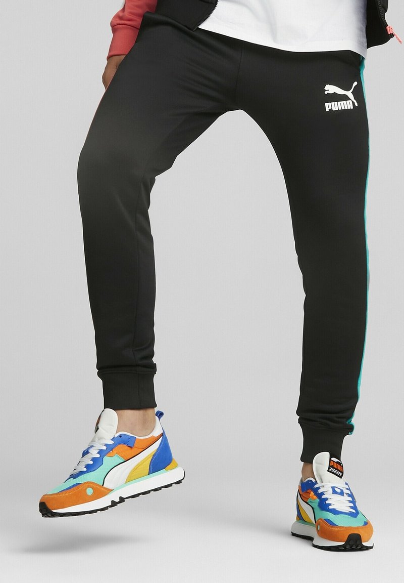 Black jogger pants with teal side stripes and a white Puma logo. Worn with multi-colored sneakers featuring blue, orange, and yellow accents.