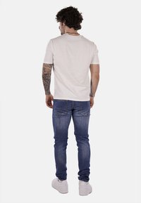 Camiseta ligera gris claro para hombre con mangas cortas, combinada con jeans de mezclilla azules y zapatillas blancas, con un diseño simple en la parte posterior y sin logotipos visibles.
