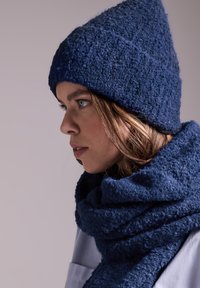 Cappello lavorato a maglia blu navy con una finitura testurizzata e una punta, abbinato a una sciarpa spessa in tinta con una consistenza morbida e pelosa.