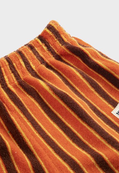 Tissu texturé rayé orange, marron et jaune avec une taille élastique froncée et une petite étiquette en tissu blanc sur le côté.