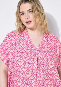 Blusa a fantasia floreale rosa con scollo a V, maniche corte e una vestibilità ampia. Presenta un motivo a rombi in diverse tonalità di rosa e bianco.
