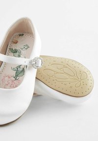 Vita ballerinas med satinfinish, prydda med en dekorativ glittrande spänne och en texturerad beige gummisula med en balettmotiv.