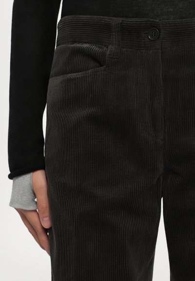 Trousers korduroi tummat dengan rusuk vertikal, dilengkapi dengan penutupan kancing dan saku samping. Dipasangkan dengan atasan hitam lengan panjang dan manset abu-abu.