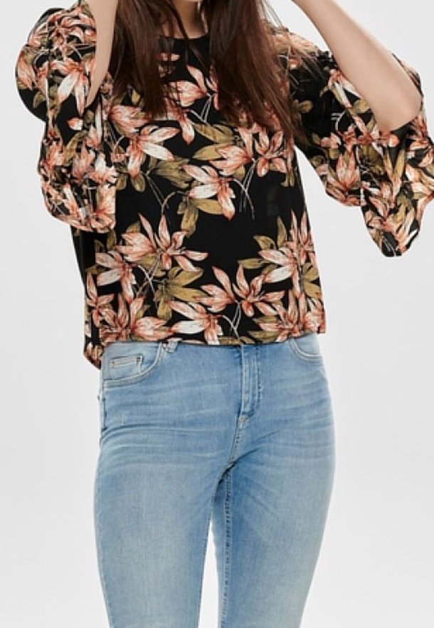 Top floreale nero con maniche a campana caratterizzato da grandi foglie arancioni e verdi, abbinato a jeans azzurri chiari. Tessuto morbido con una vestibilità comoda.