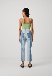 Zeleni rebrasti kratki top v kombinaciji z dvobarvnimi denim hlačami, ki imajo svetlo in temno modre načrte ter klasične zadnje žepke. Ravni sandali.