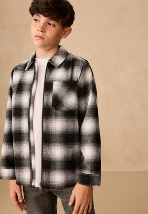 Sort og hvid ternet flannelskjorte med en frontlomme, lynlåslukning og spids krave. Båret over en hvid t-shirt.