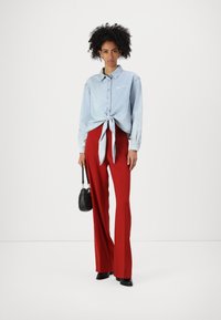 Ljusblå denimskjorta med knut framtill, i kombination med höga röda vida byxor. Har en liten logotyp och en svart handväska.