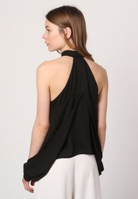 Top negro sin mangas con escote halter, espalda suelta y tela suave. Presenta hombros descubiertos y una silueta fluida.