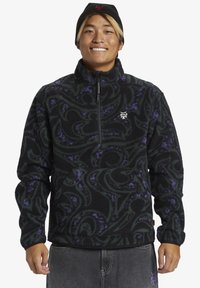 Schwarzer Fleece-Pullover mit wirbelnden grünen und lila Mustern, halbseitigem Reißverschluss und gerippten Bündchen. Verfügt über ein kleines Logo auf der Brust.