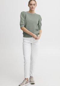 Lysegrønn kortermet genser med strukturert strikk, ribbestrikkede mansjetter og kant, sammen med hvite slim-fit bukser og beige joggesko.