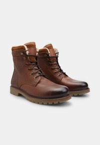 Pár hnedých kožených čižiem na šnurovanie s kožušinovým podšívkou a robustnými gumovými podrážkami na bielom pozadí.