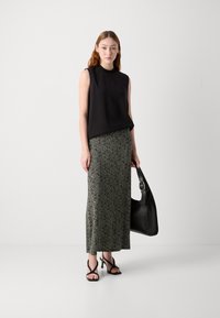 Top negro sin mangas combinado con una larga falda verde estampada. Los accesorios incluyen un gran bolso negro y sandalias de tacón negro con tiras.