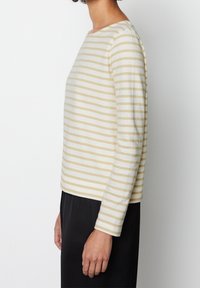 Gestreepte longsleeve top in crème en lichtgeel, met een bootnek, zachte textuur en een relaxte pasvorm. G gedragen over zwarte broek.