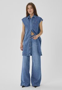 Jeans haljina s ovratnikom, kratkim rukavima, kopčanjem na dugmad i prednjim džepom, u kombinaciji s širokim trapericama svijetloplave boje.