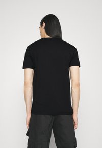 Svart t-shirt med kort ärm och rund hals, tillverkad av bomull. Har en enfärgad baksida. Kombinerad med mörka cargobyxor.