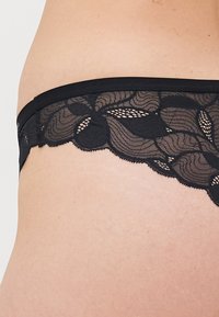 Primo piano di un cinturino di lingerie in pizzo nero con motivo floreale su pelle nuda.