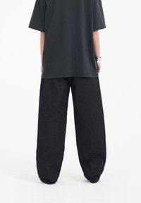 Svarta vida byxor med en slät texture, ihopkopplade med en löst sittande mörkgrå t-shirt. Avslappnad, ostrukturerad design.