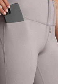 Leggings gris clair en matière extensible, avec une poche latérale contenant un smartphone gris foncé. De subtils détails de couture sont visibles.