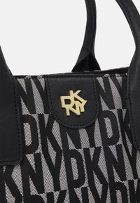 Czarna torebka wykonana z teksturowanej tkaniny z wzorowanym logo DKNY. Złote akcenty na górnej klapce podkreślają odważny design.